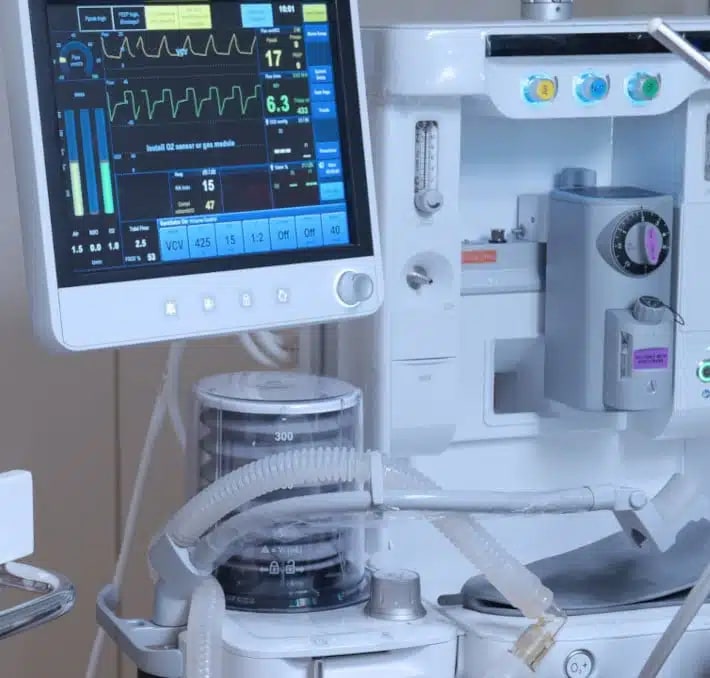 A close-up view of a medical ventilator and monitoring equipment displaying patient vital signs in a hospital setting.