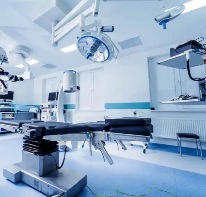 Modern operating room with advanced medical equipment, surgical lights, monitors, and an empty adjustable operating table.